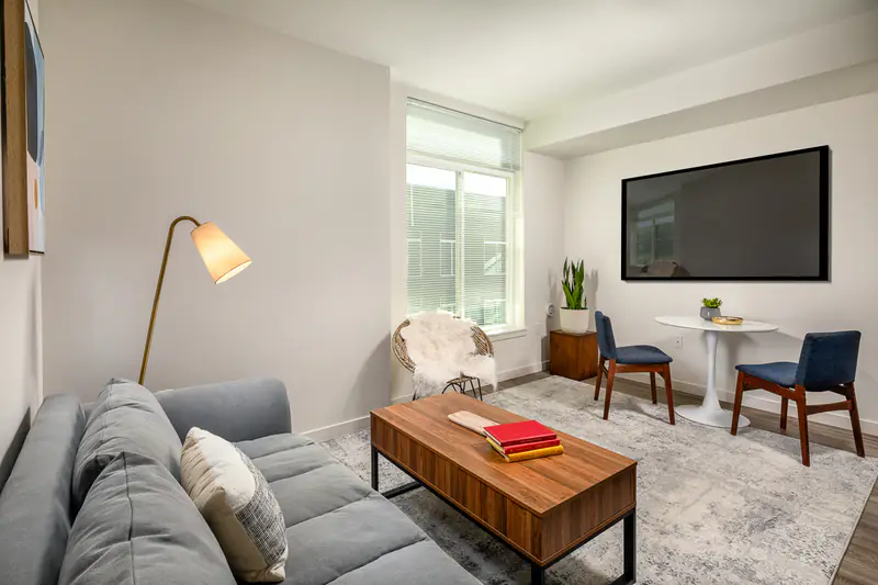 Apartments in Tacoma, WA, with In-Unit Washer and Dryer - Hailey - Bright Living Room With Gray Sofa, Wood Coffee Table, Dining Area, Large Window, And Wall-Mounted Television.